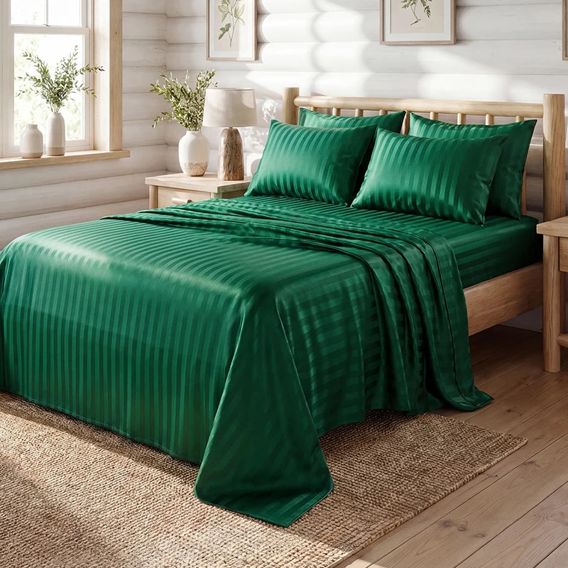 A dark emerald green satin bedding set with striped duvet and pillows on a wooden bed.