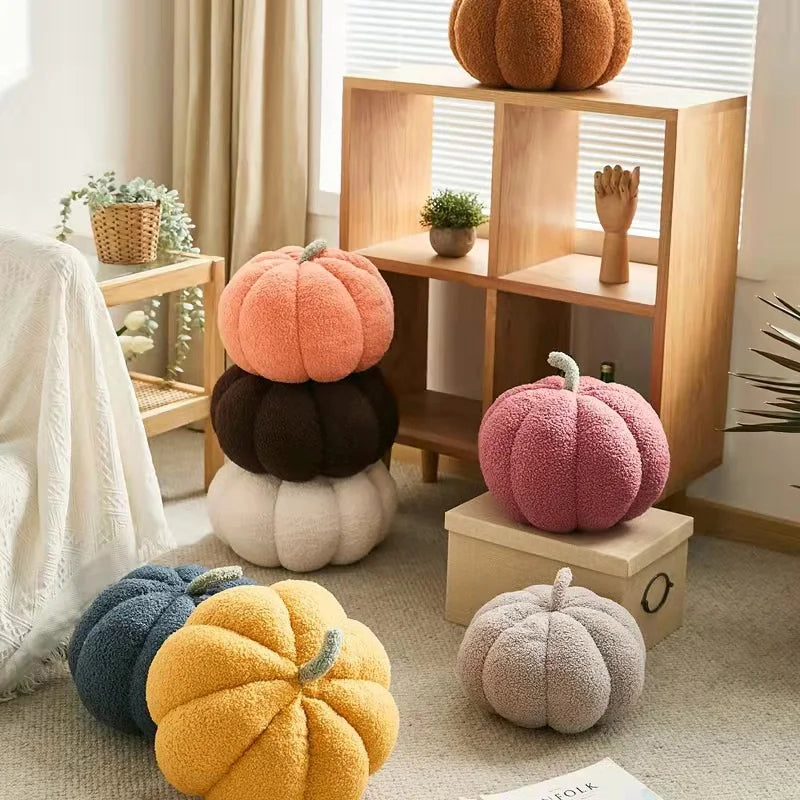 A collection of various orange, pink, and yellow plush pumpkins displayed on a wooden shelf.