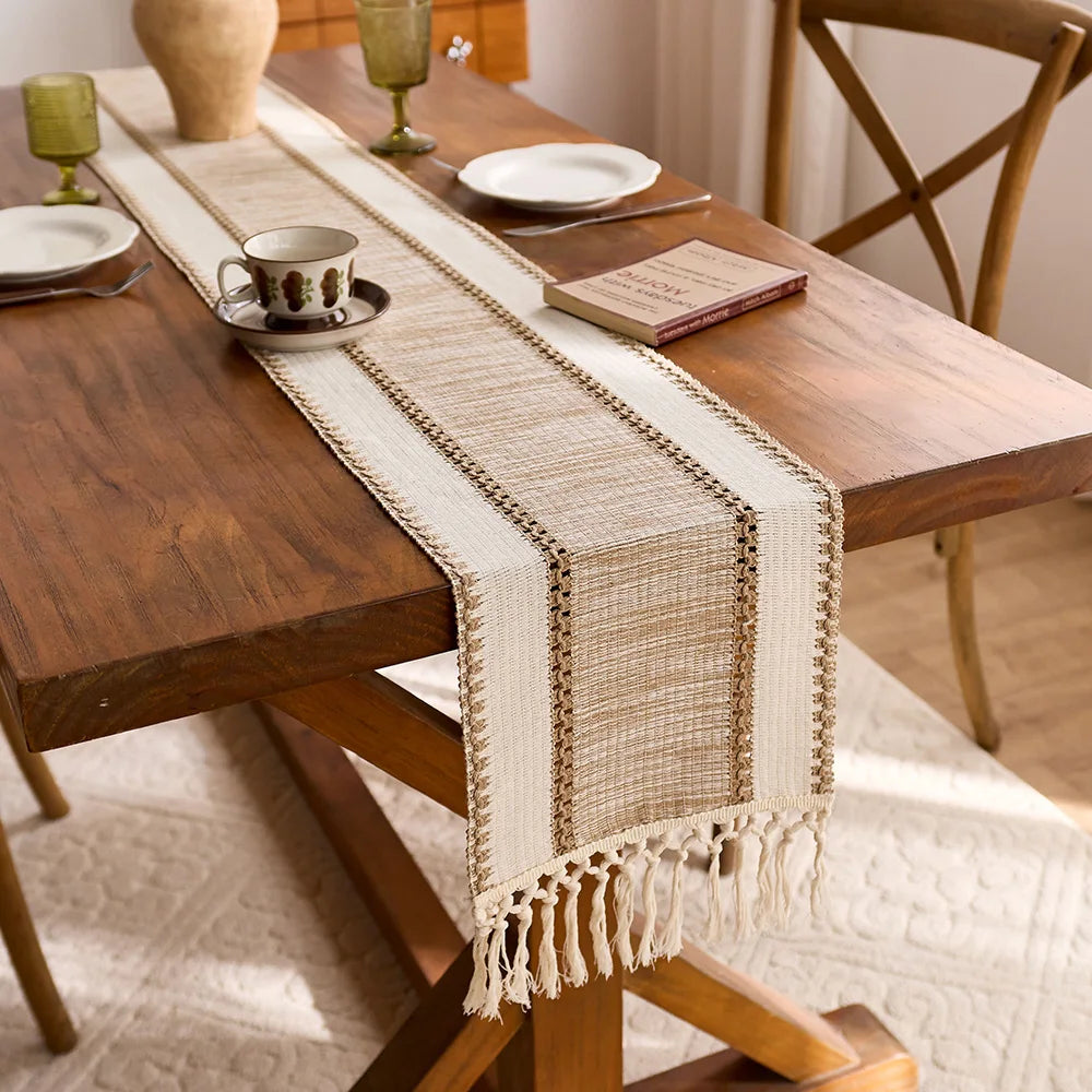 A woven beige tassel table runner with macrame design is placed on a wooden dining table.