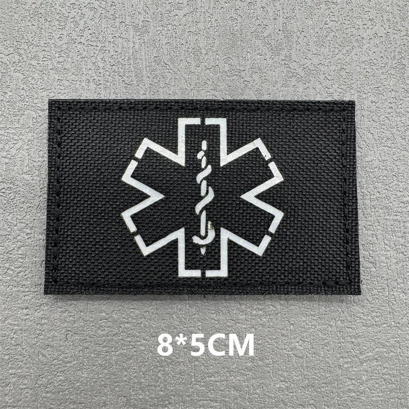 Black fabric patch with a white medical cross symbol embroidered on it