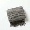 A gray oversized knitted tassel throw blanket with a fringed edge.