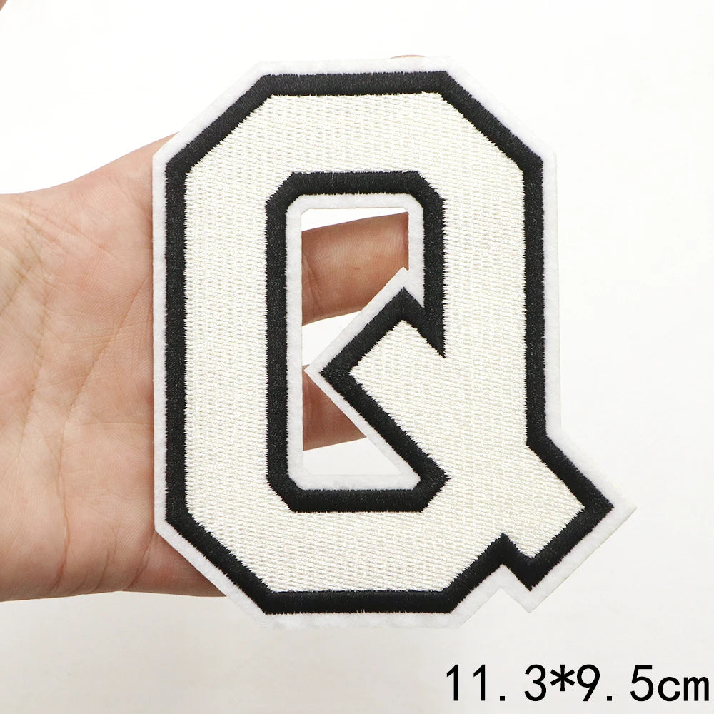 A white letter Q patch with a black outline is held in a hand.