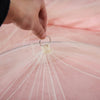 A hand is adjusting a section of a pink 360° Princess Dome mosquito net fabric.