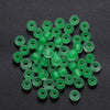 A pile of small, bright green glass seed beads scattered on a dark surface.