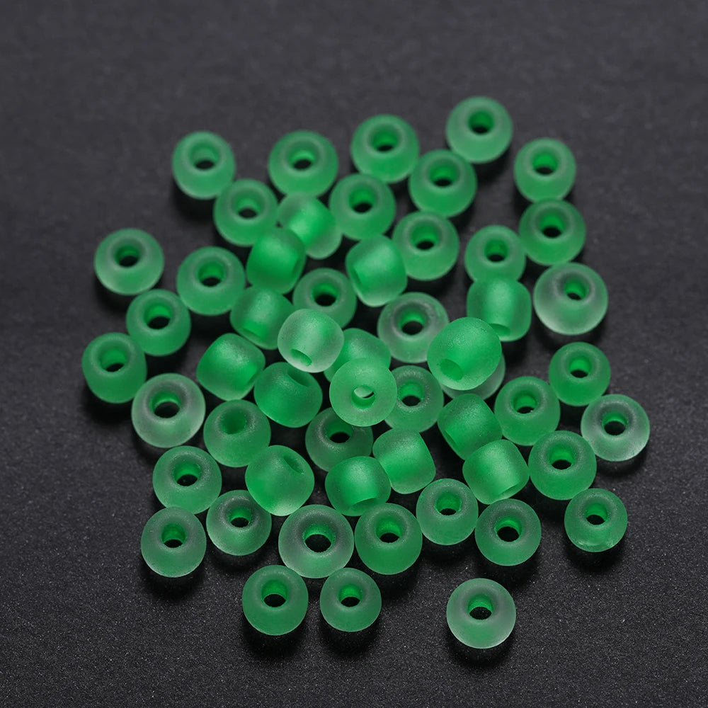 A pile of small, bright green glass seed beads scattered on a dark surface.