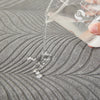 A hand pours liquid from a clear bottle onto a textured gray fabric surface.