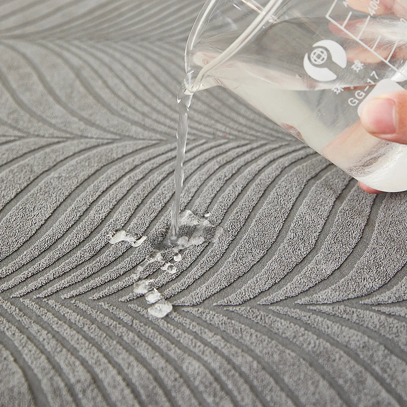 A hand pours liquid from a clear bottle onto a textured gray fabric surface.