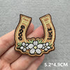 A hand holds a Western cowboy embroidered iron-on patch featuring the words GOOD LUCK surrounded by floral embroidery.