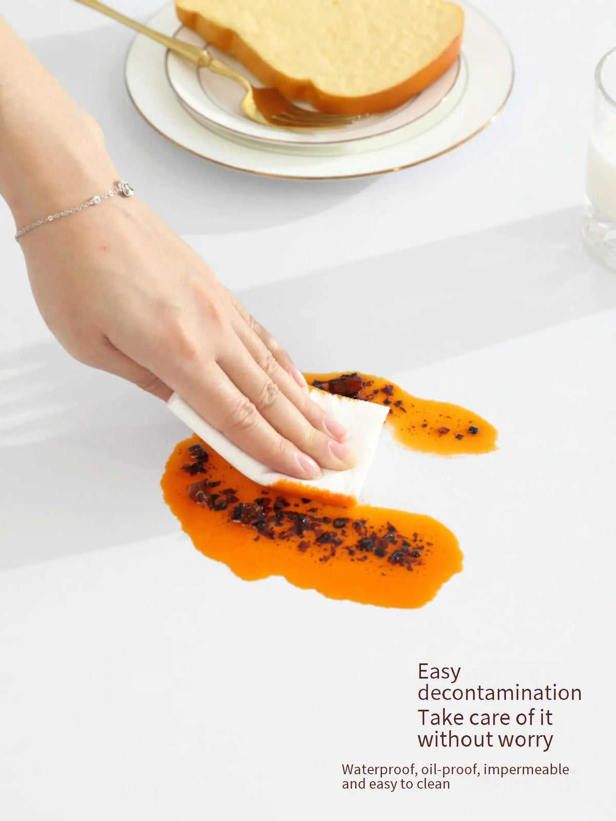 A hand wipes orange food from a marble table cloth for easy decontamination.