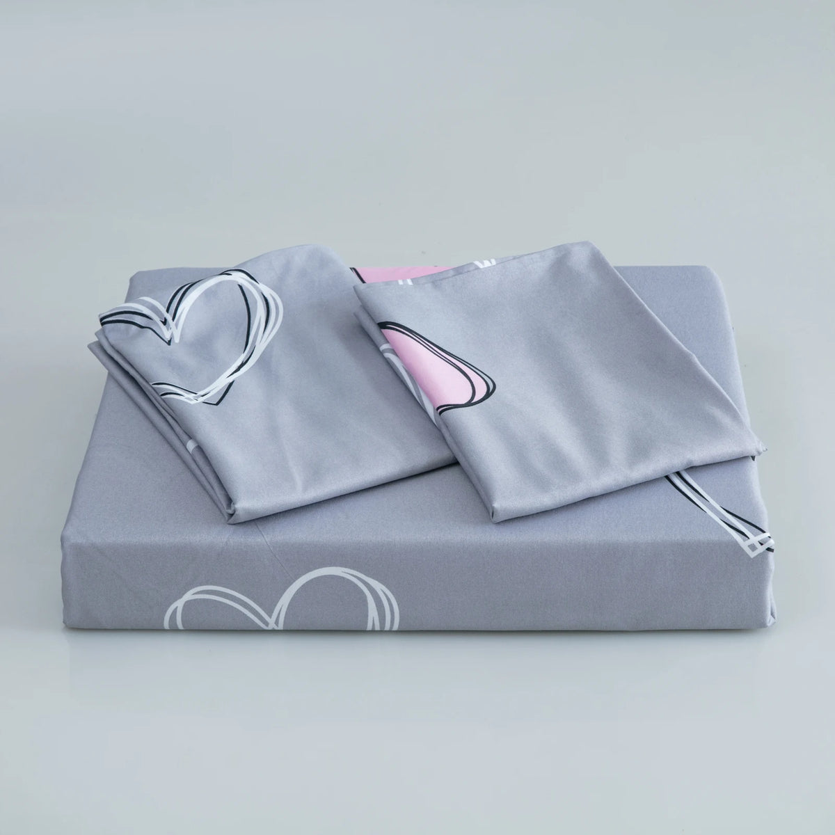 A gray bedding set featuring a duvet cover and pillowcases with pink heart prints.