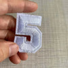A hand holds a white embroidered number 5 patch for apparel.