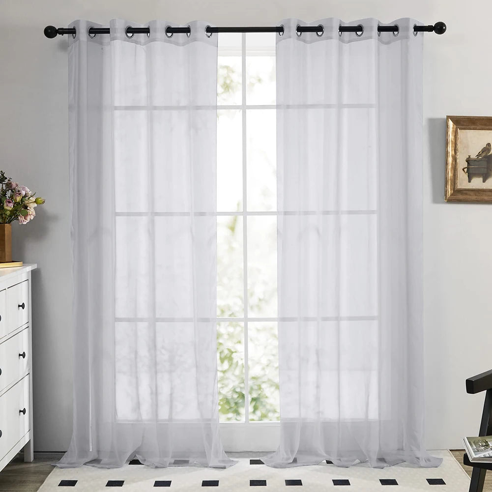 White sheer tulle window curtains hanging in a window frame with a black rod and gathered fabric.