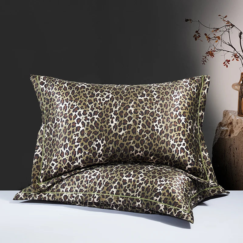 A pair of leopard print silk satin pillowcases displayed on a white surface against a dark gray background.