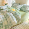 A light green duvet cover with white and blue patterned fleece throws and pillows on a bed.