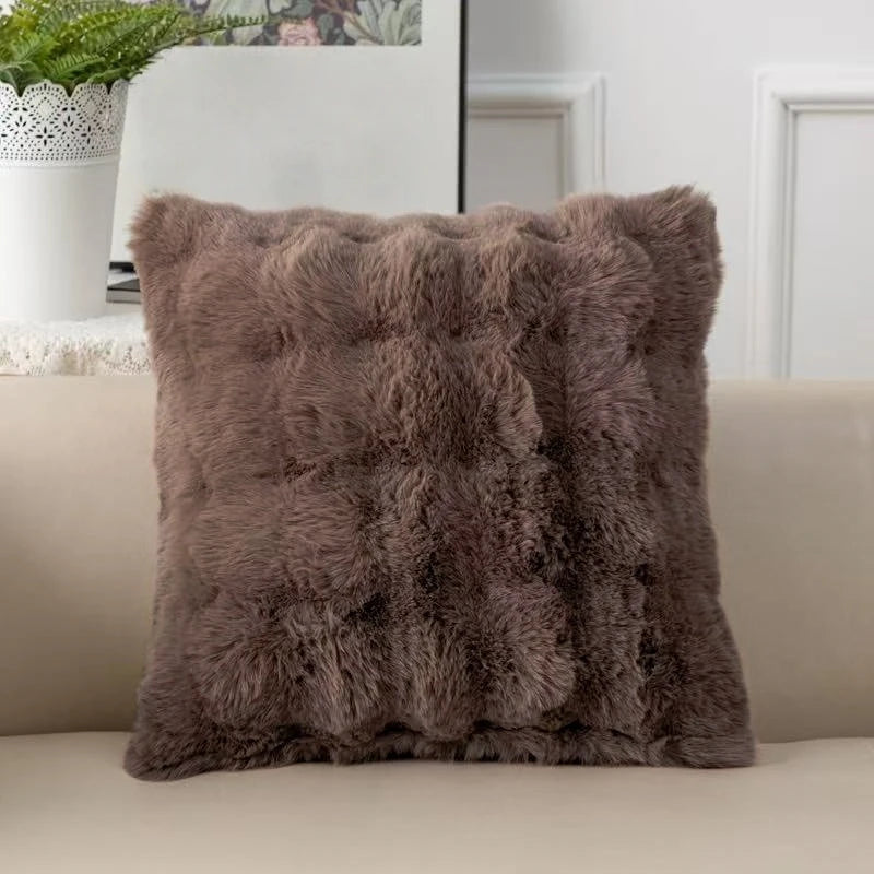 A plush faux rabbit fur decorative throw pillow in a warm brown color resting on a light-colored sofa.