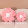 A pink plush daisy flower throw pillow with a white center displayed on a light colored surface.