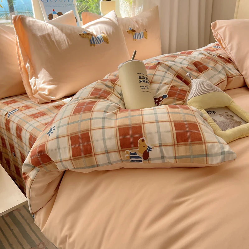A cozy bed with a plaid bedding set featuring cartoon embroidery and a reusable tumbler.