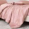 A soft pink luxury bamboo duvet cover set draped on a bed with a gray carpet.