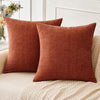 A solid terracotta orange chenille throw pillow resting on a light beige sofa.