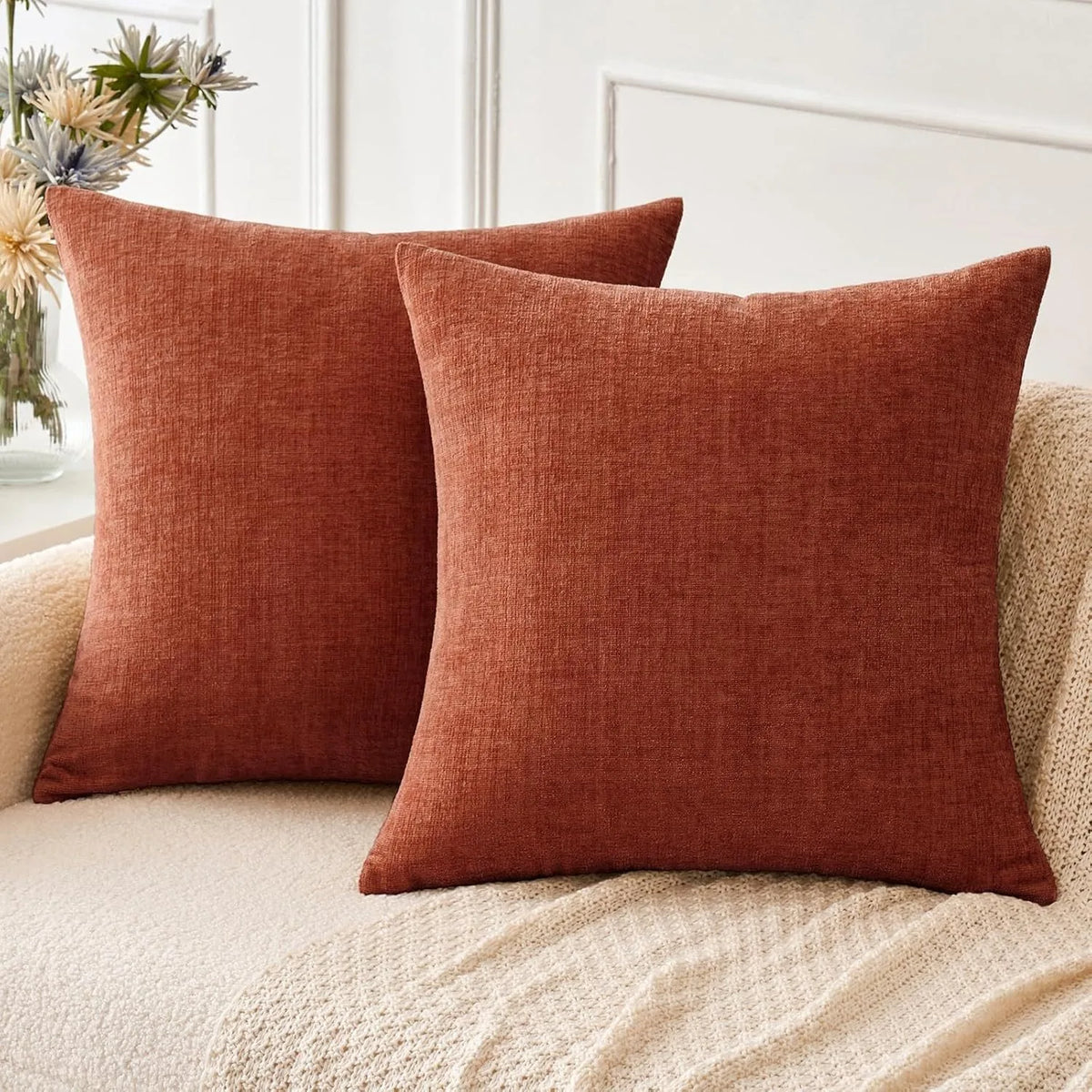 A solid terracotta orange chenille throw pillow resting on a light beige sofa.