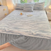 A light gray plush bed skirt linen set with striped bedding and pillows on a bed.