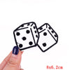 A hand holds two embroidered black and white polka dot dice patches, measuring 8x6.2 cm.