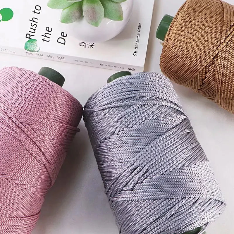 Three skeins of colorful crochet ice rope yarn in pink, gray, and brown are displayed next to a book.