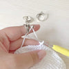 A hand holds a white crochet ring with silver tension rings and a needle.