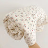 A rolled floral print muslin blanket for baby in off-white with red and blue floral patterns.