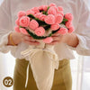 A person holds a hand knitted floral rose bouquet throw blanket with pink roses and green leaves.