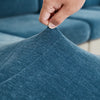 A hand is adjusting a textured blue stretchable chenille sofa cushion cover.
