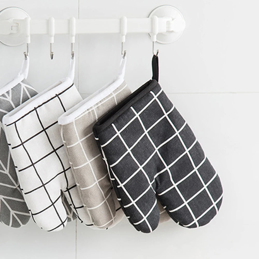 A pair of black and white checkered heat-resistant kitchen oven gloves hanging on a white rack.