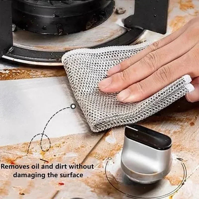 A hand is using a thickened double-sided metal scouring dish cloth to remove oil and dirt from a surface.