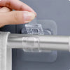A hand is using a self-adhesive curtain rod clip to secure a rod onto a wall or window frame.