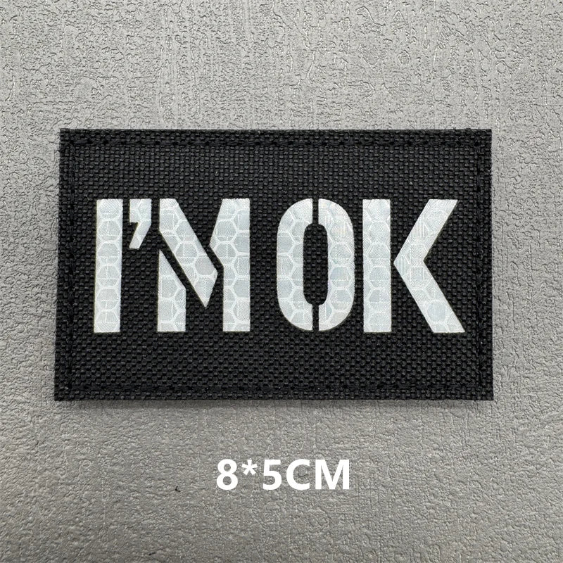 Black embroidered patch with the text I'M OK in white lettering on a gray background.