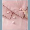 A hand is holding a pink fabric, showing several round silicone quilt clips sewn onto the material.