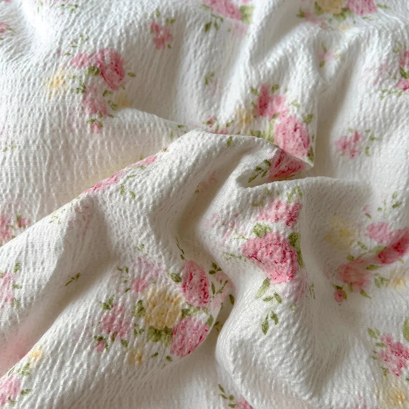 Close-up of white fabric bedding with a pink and yellow floral pattern, showing soft folds.