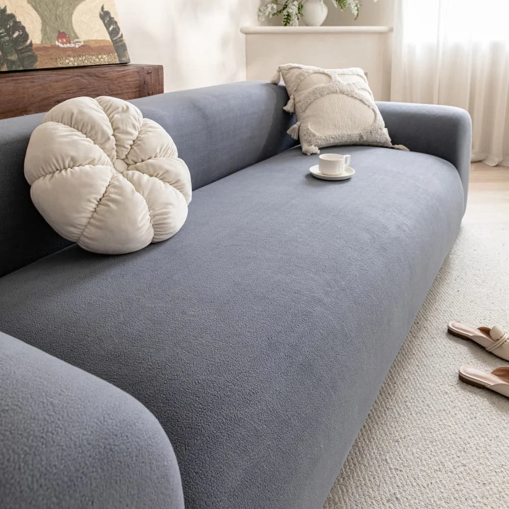 A soft gray quilted sofa cover with a cream cushion and a white cup rests on a light rug.