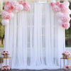 A white tulle backdrop decorated with pink floral pom-poms and draped sheer fabric for an event.