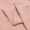 Close-up of a pink cotton knit baby blanket showing the texture and stitching detail.