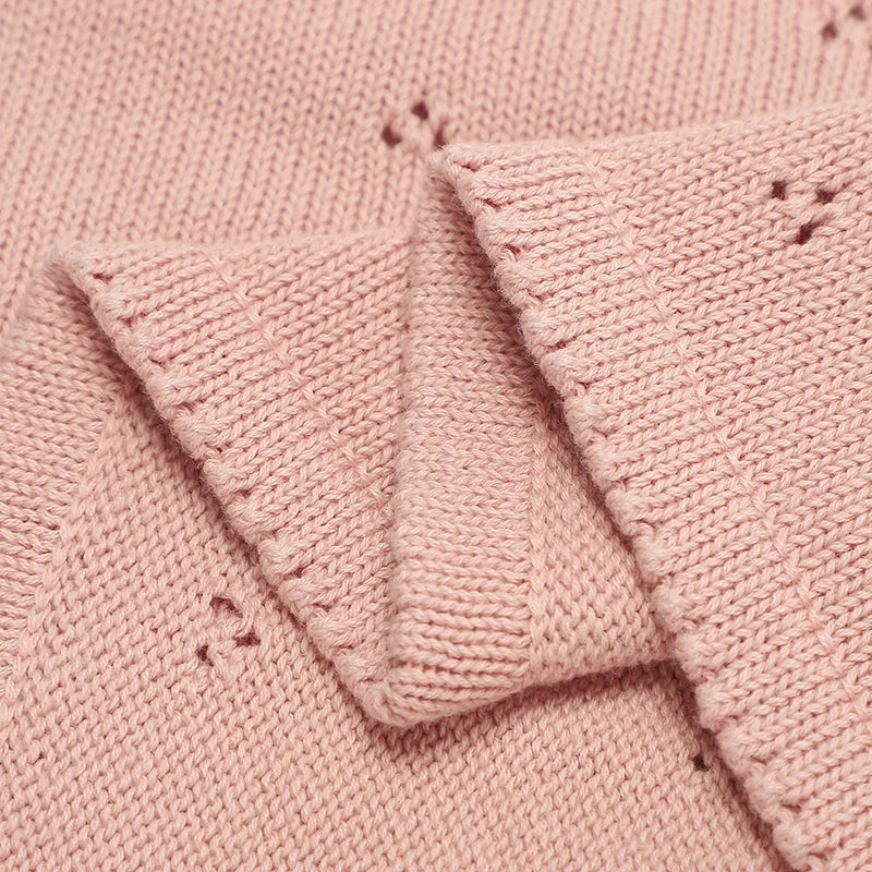 Close-up of a pink cotton knit baby blanket showing the texture and stitching detail.