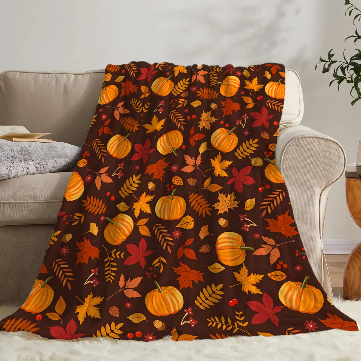 A dark orange and red autumn leaf pattern fleece throw blanket draped over a light colored sofa.