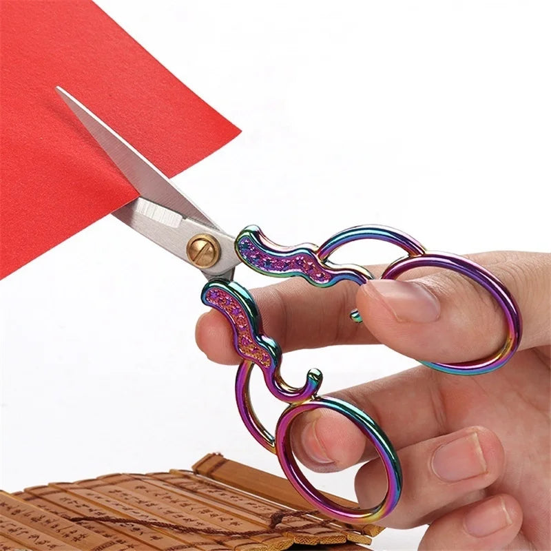 A pair of vintage stainless steel sewing scissors with iridescent purple and green handles resting on a wooden surface.