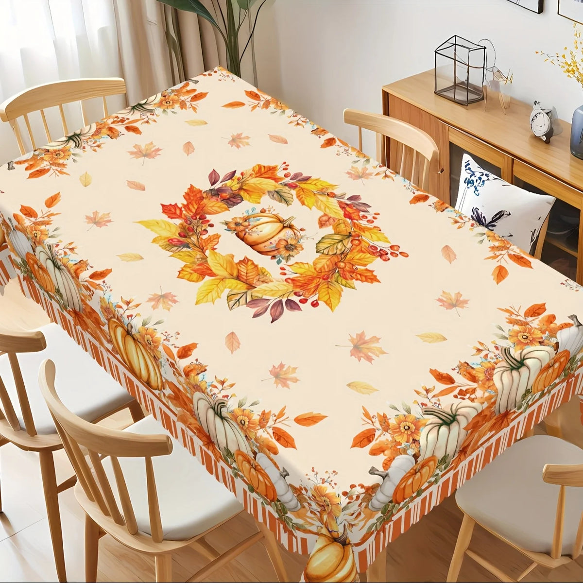 Fall harvest tablecloth featuring orange pumpkins and maple leaves on a wooden dining table.