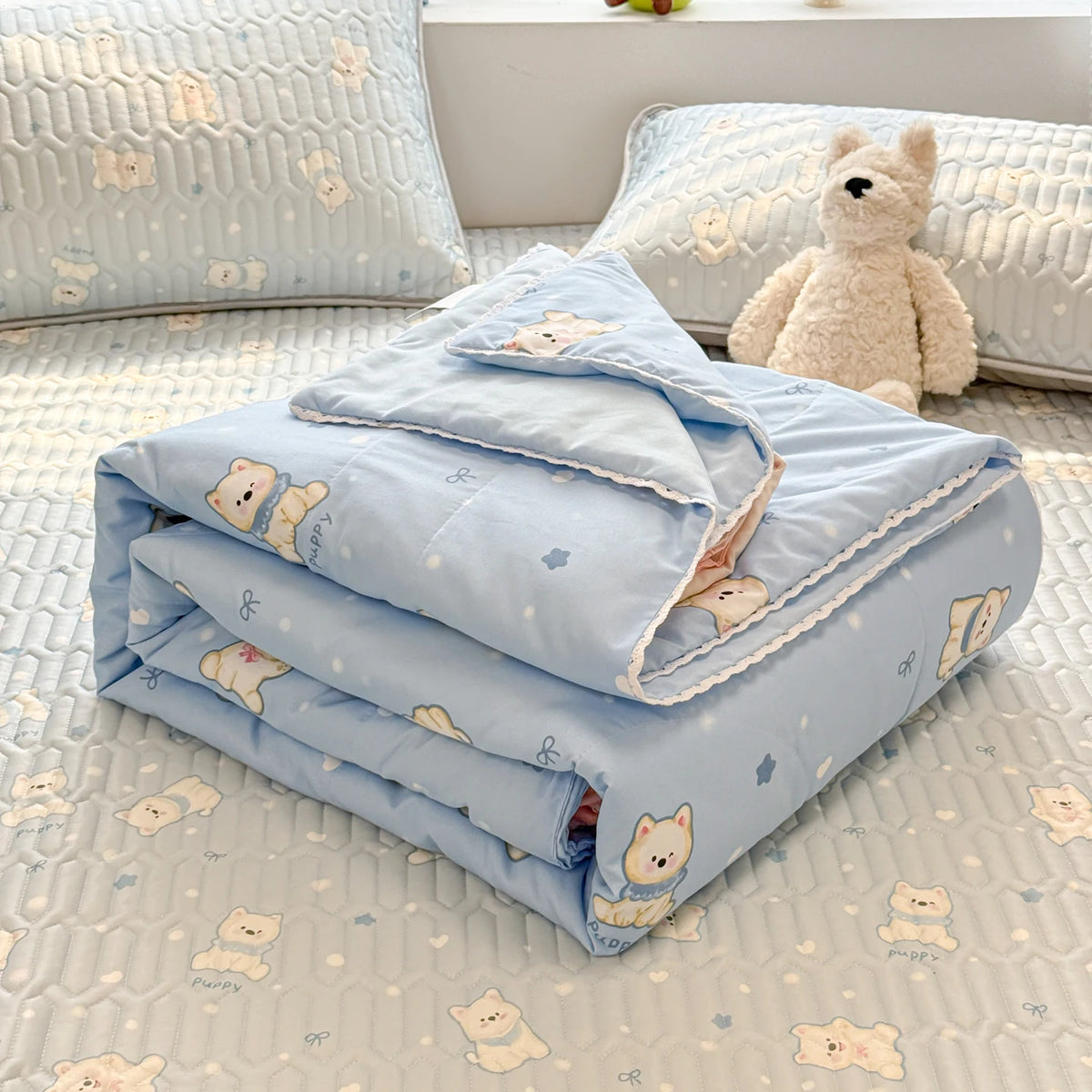 Light blue quilted blanket with a pattern of small cream-colored bears and stars resting on a white surface.