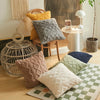 A collection of textured and plaid cushions displayed on a light wooden floor.