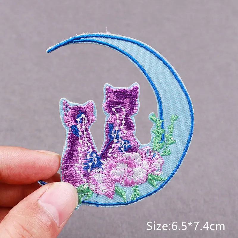 Embroidered patch featuring two purple cats on a light blue crescent moon background