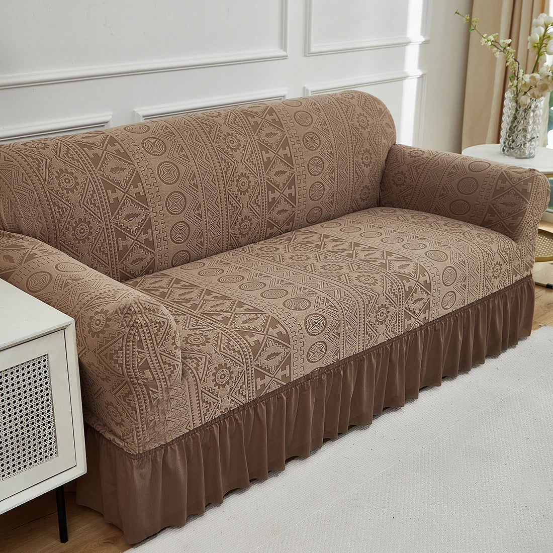 A tan jacquard stretch sofa cover draped over a beige sofa in a bright room.