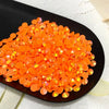 A pile of orange-red AB resin flatback rhinestones scattered on a black plate.