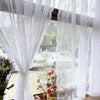 White floral embroidery sheer curtain hanging in a window with blurred outdoor view